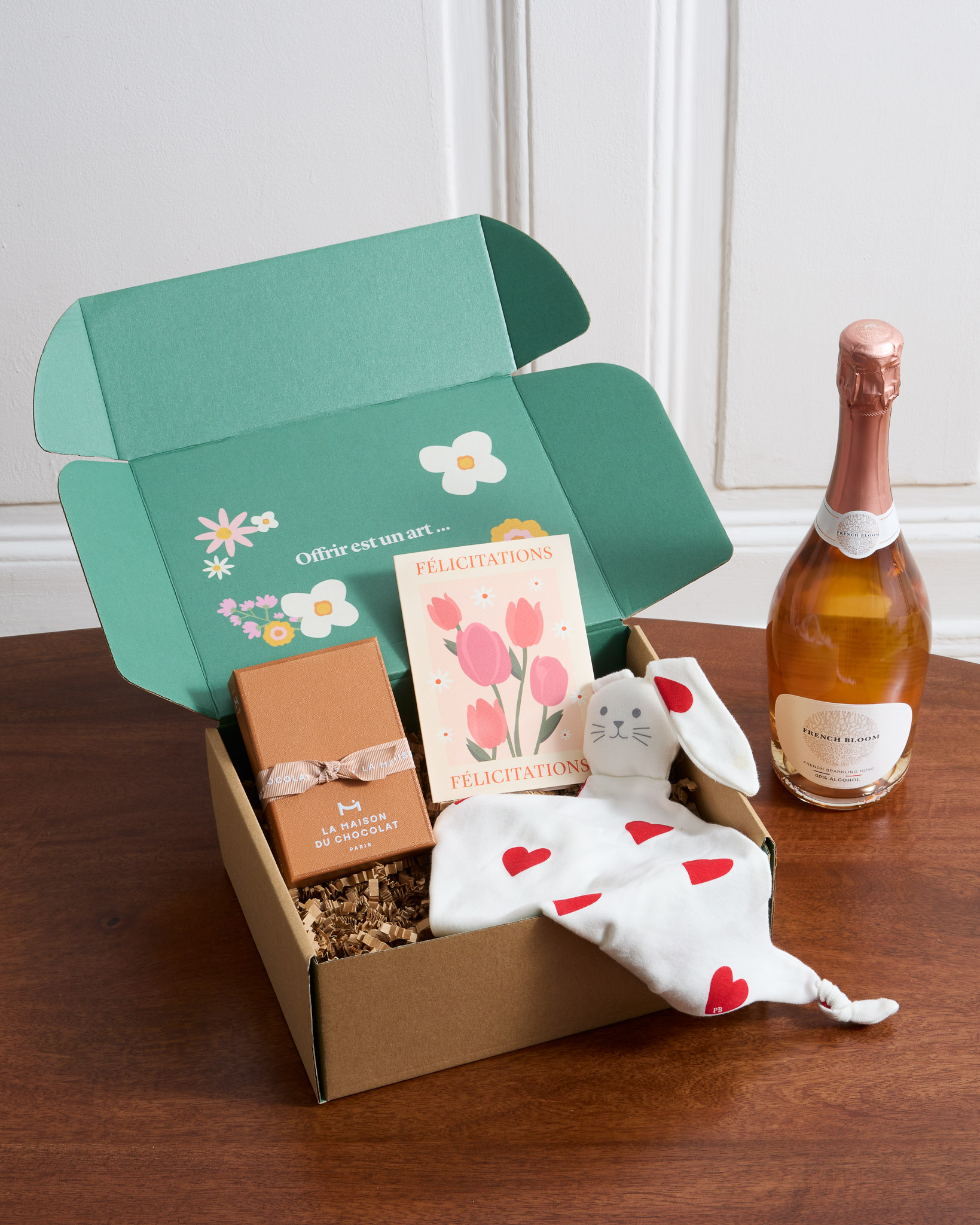 Ce coffret contient : une bouteille de rosé sans alccol French Bloom, un doudou Petit Bateau, un coffret de pépites pralinées Maison du Chocolat et une carte illustrée